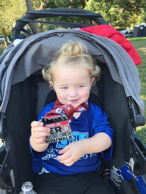 A young child in a stroller holding up a medal from the ZERO Prostate Cancer Run/Walk