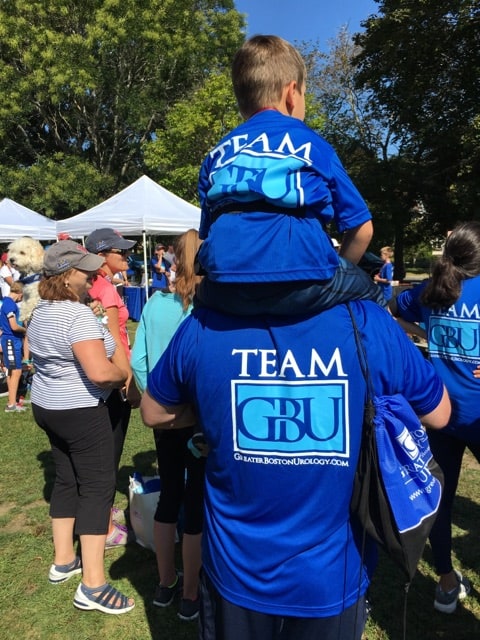 A man carrying a child on his shoulder, both are wearing a Team GBU t-shirt