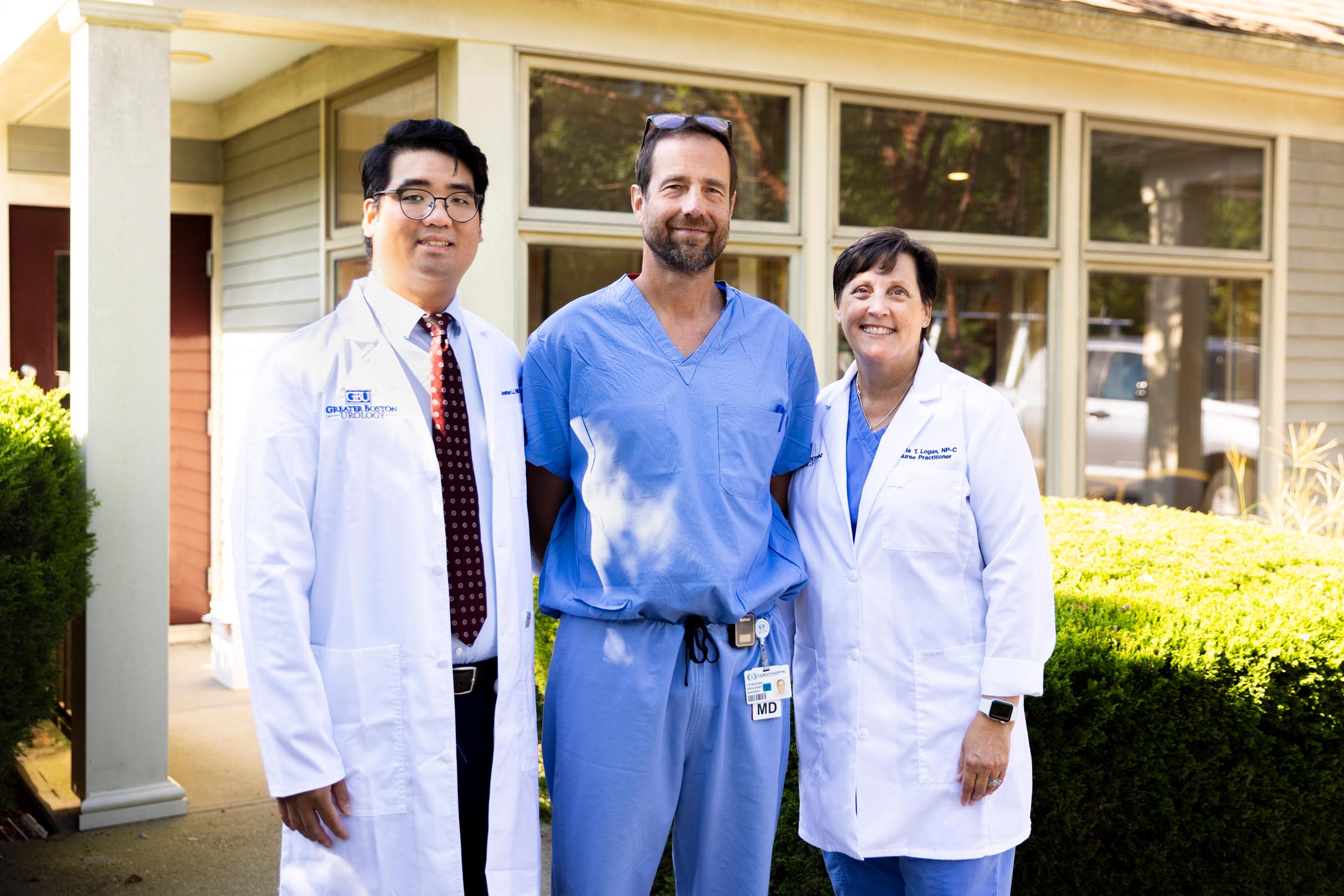 picture of three medical professionals in blue scrubs and white lab coats standing in front of a medical building, Dr Li, Dr. Bleiler, and Olivia Logan, NP