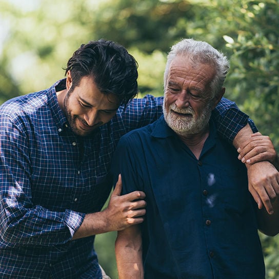 A younger man with is arm around an older man, walking together