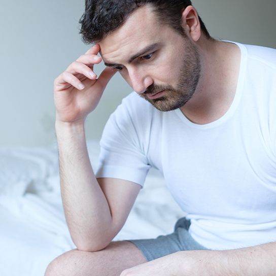 Man sitting on bed looking distraught