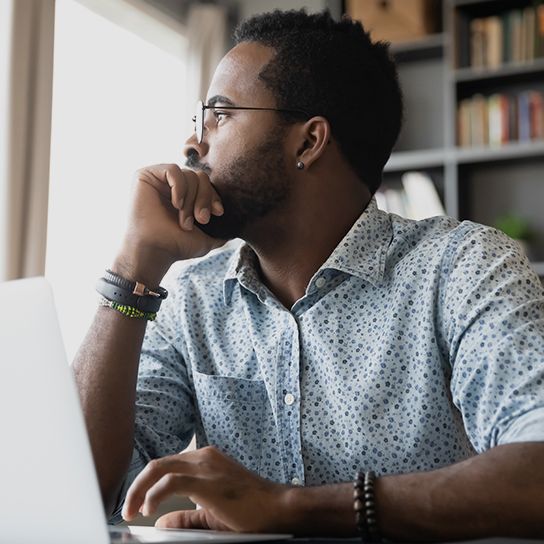 Man sitting in front of laptop looking to the side and resting hand on his hand