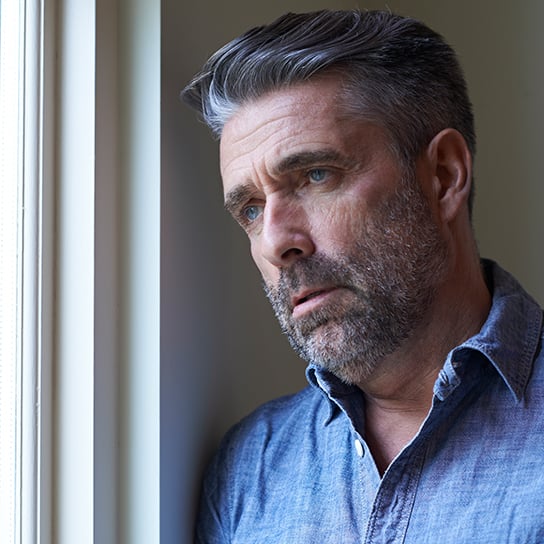 Older man looking distraught and looking out a window