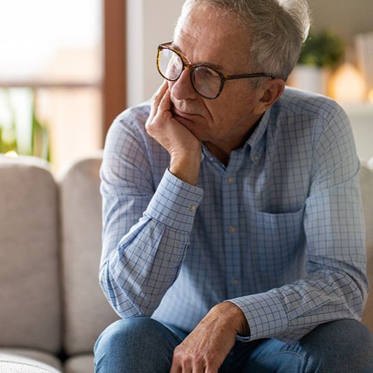 Older man sitting on the edge of a couch, leaning forward and rest his chin on his hand