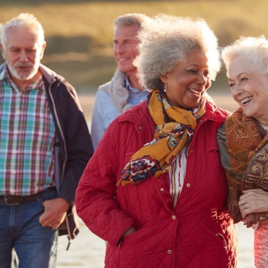Two woman linking arms and laughing while two men walk behind them, talking