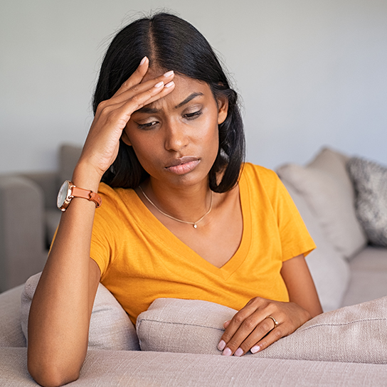 Woman sitting at edge of couch, looking distraught 
